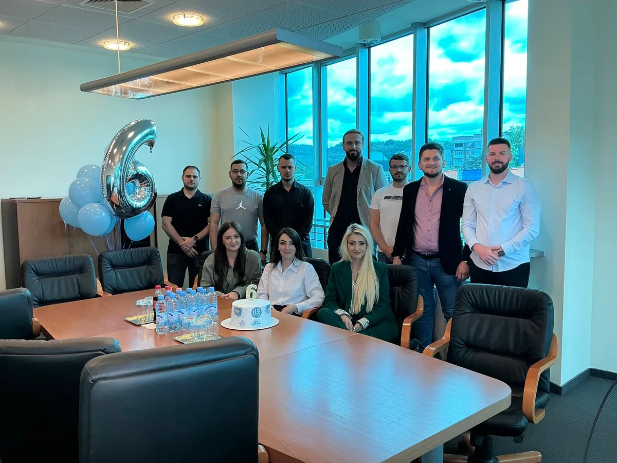 A group gathered around a celebration cake and balloons at the Obscale office.