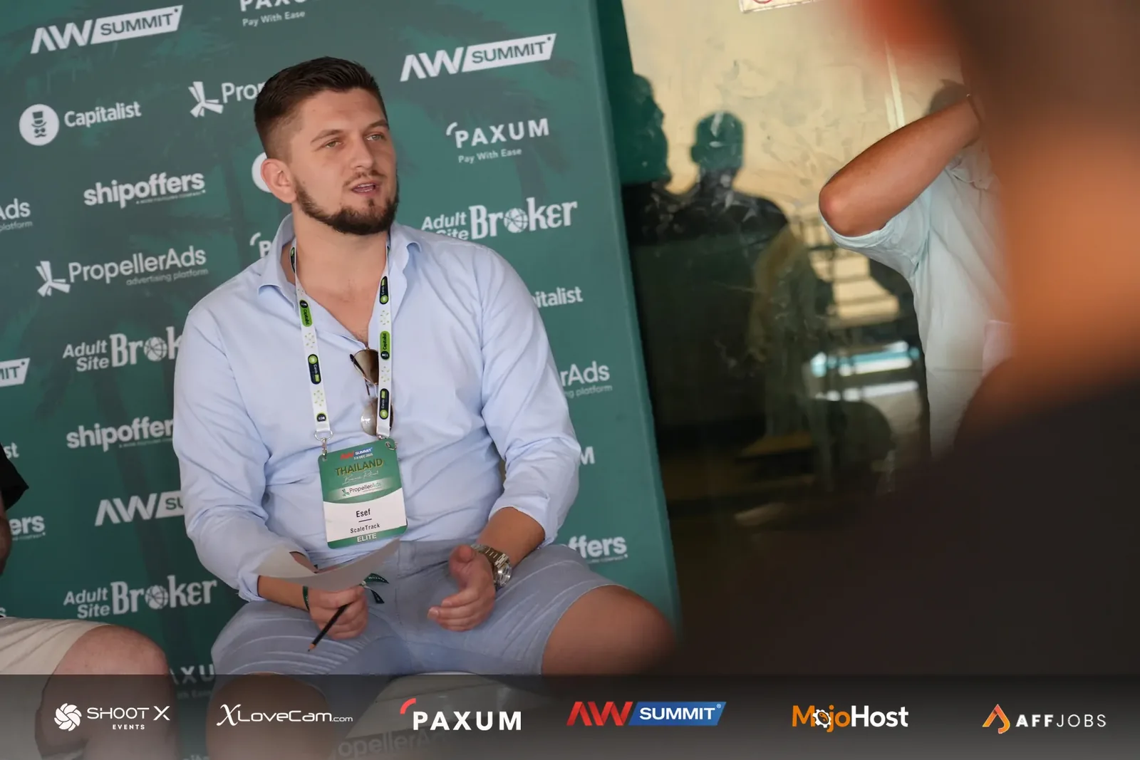 A seated attendee holding notes in front of an AW Summit backdrop.