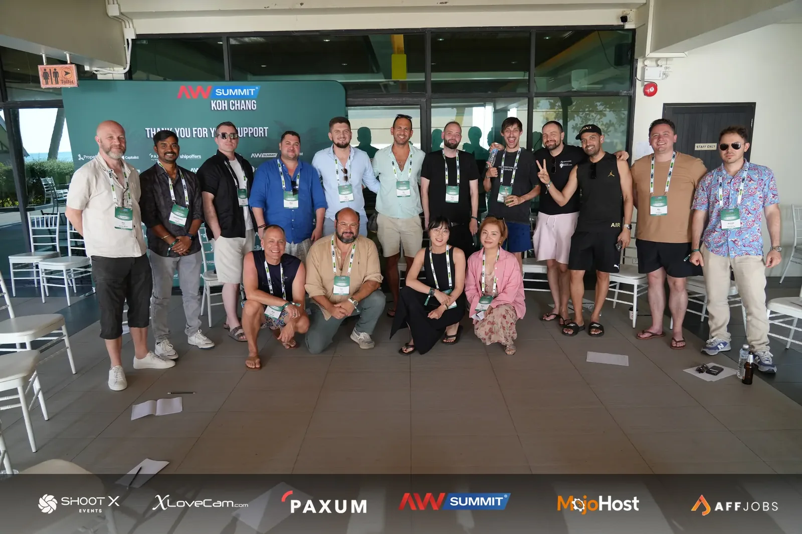 A group of conference attendees posing in front of an AW Summit Koh Chang backdrop.