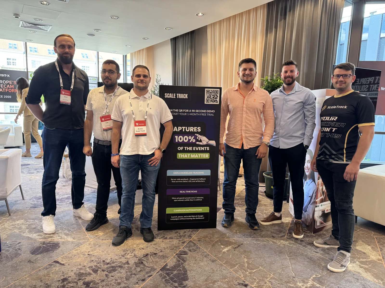 Six conference attendees standing around a ScaleTrack display banner.